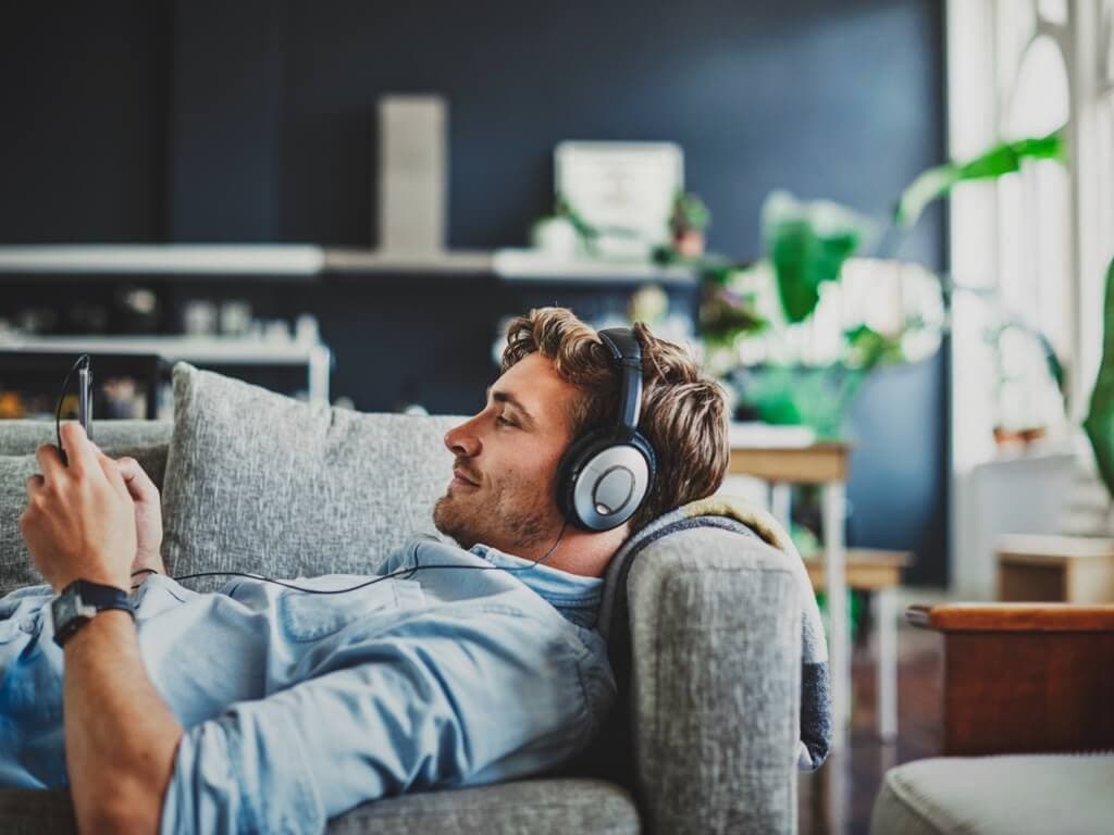 Muškarac se opušta na kauču, sluša glazbu kroz slušalice, s mirom na licu