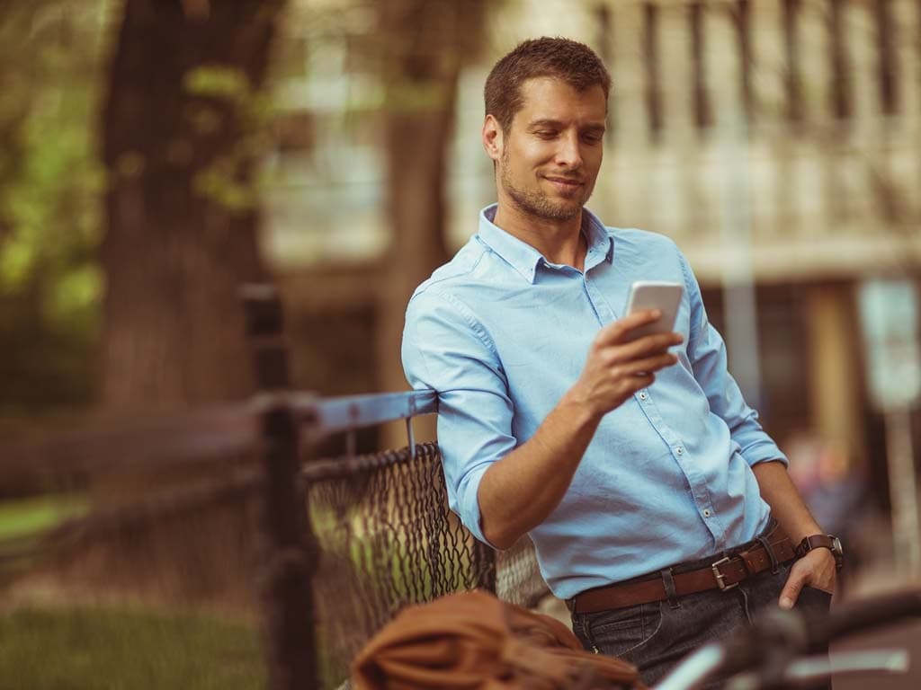 Muškarac stoji kraj ograde, usredotočen na svoj telefon, s zamišljenim izrazom lica