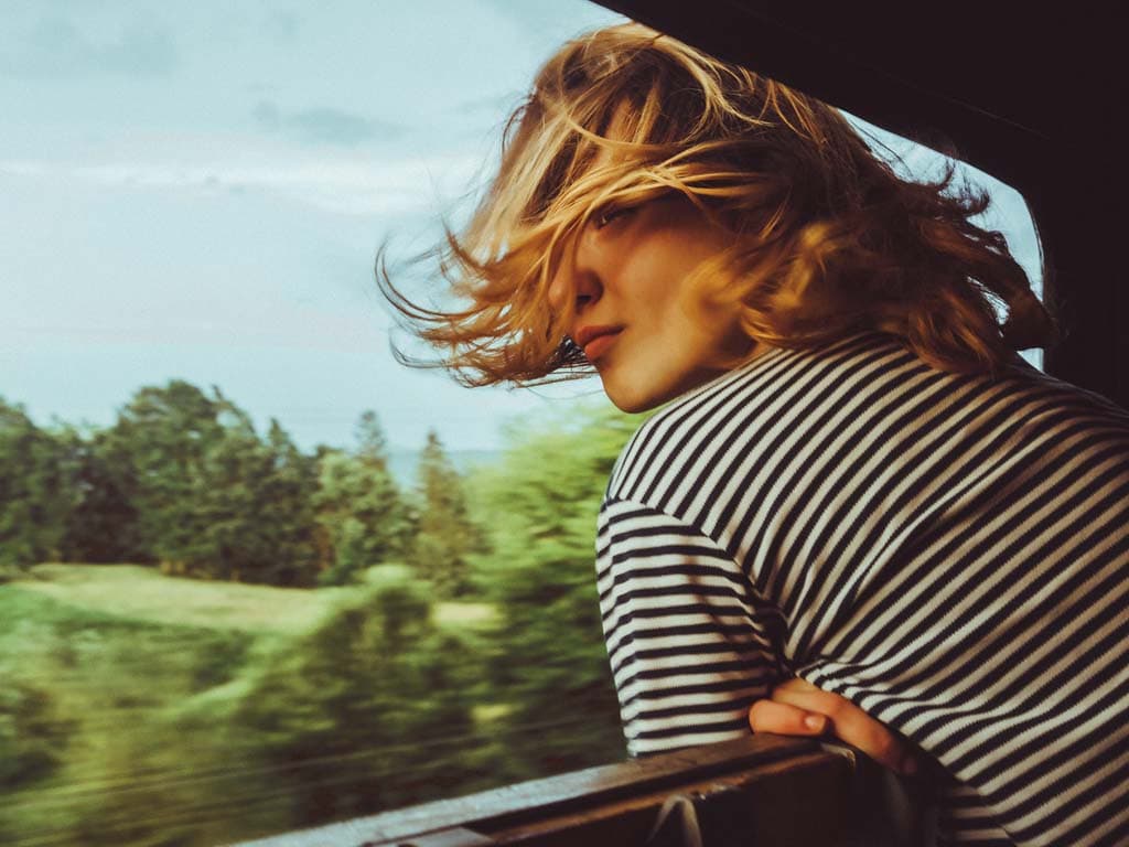 Žena zamišljeno gleda kroz prozor vlaka u pokretu, promatrajući krajolik koji prolazi