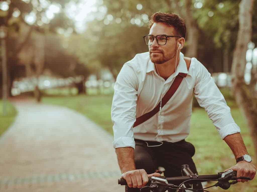 Muškarac s naočalama vozi bicikl stazom, uživajući u sunčanom danu u prirodnom okruženju