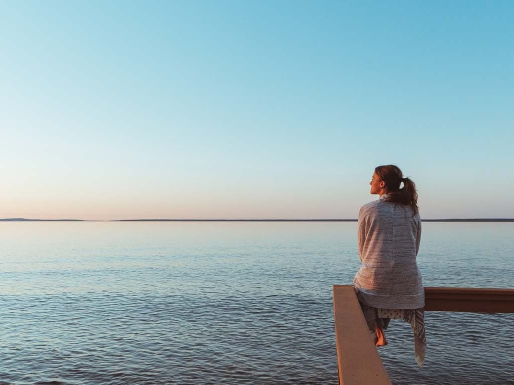 Žena sjedi na molu, gledajući prema moru tijekom živopisnog zalaska sunca