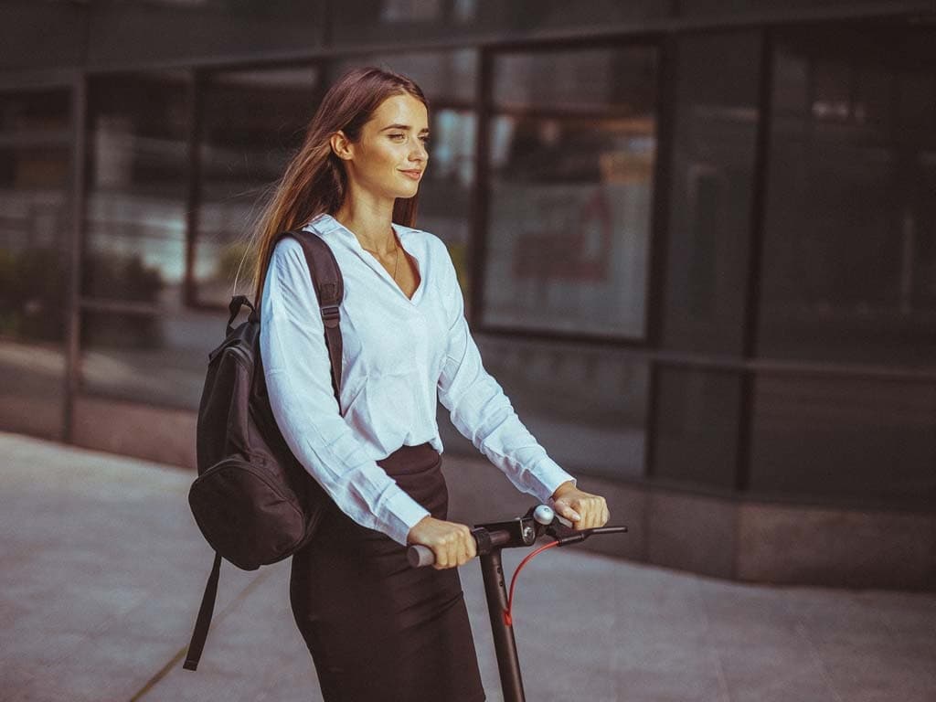 Žena u poslovnom odijelu vozi skuter, ilustrirajući dinamičan pristup putovanju na posao u profesionalnom okruženju