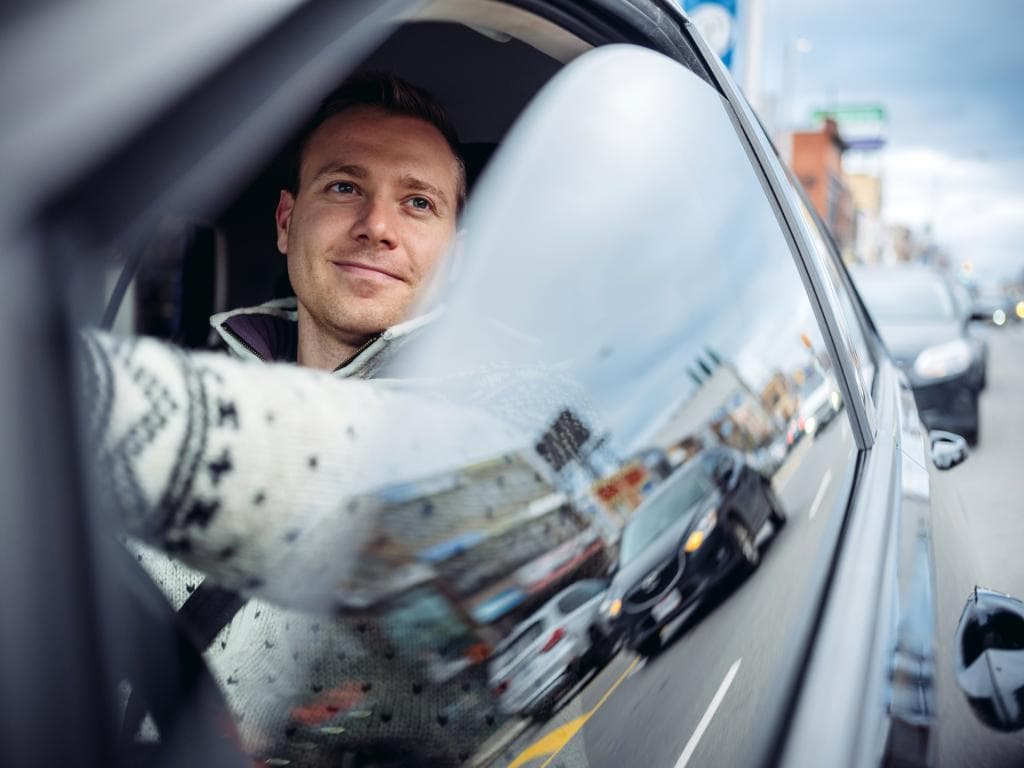 Muškarac vozi automobil dok gleda kroz prozor, usredotočen na krajolik vani