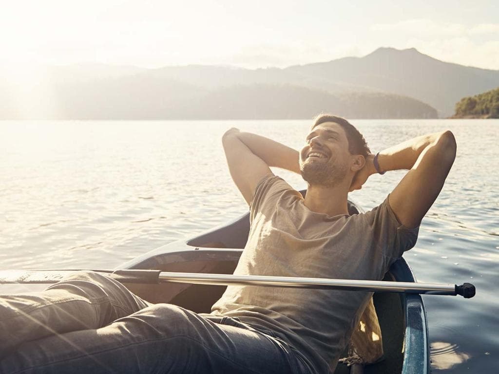 Muškarac se opušta u kanuu na mirnom jezeru, okruženim tihim vodama i udaljenim drvećem