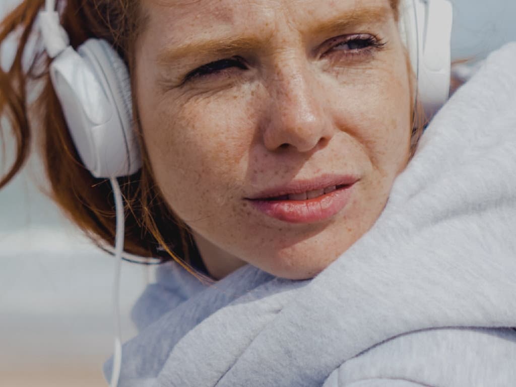 Žena s slušalicama opušta se na plaži, uživajući u suncu i zvuku valova