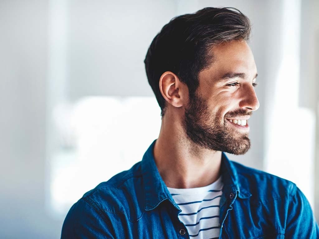 Bradat muškarac u plavoj košulji toplo se smiješi, izražavajući osjećaj sreće i prijateljstva