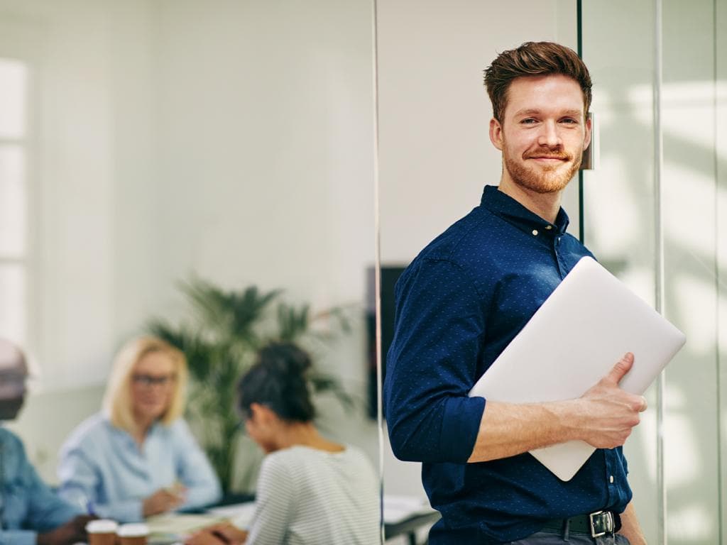 Muškarac u uredu drži prijenosno računalo, izgleda usredotočeno i angažirano u svom poslu