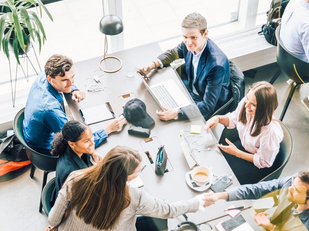Raznolika skupina ljudi sjedi oko stola, svaki koristi prijenosno računalo tijekom suradničke radne sesije